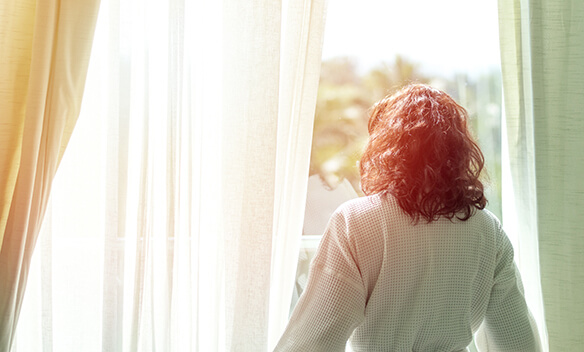 Woman watching the sunrise through her window